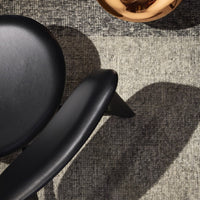 Black chair on a textured gray rug with a shiny copper bowl, creating a stylish, modern contrast.