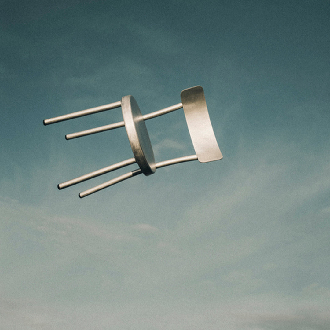 Silver metal chair against a blue sky, featuring a smooth, minimalist design with sleek lines and a modern aesthetic.