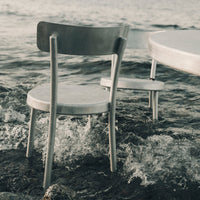 Silver metal chair with a minimalist design, featuring a smooth finish, set against a serene, watery background.