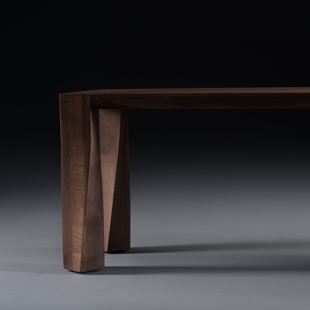 Dark walnut wood table with a smooth finish and unique, angled leg design against a gradient gray background.