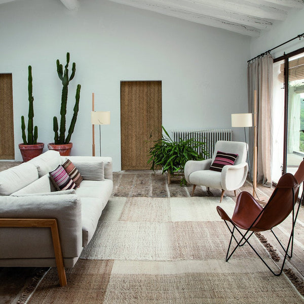 Modern living room featuring neutral tones, vibrant green plants, and striped burgundy and cream patterns on cushions.