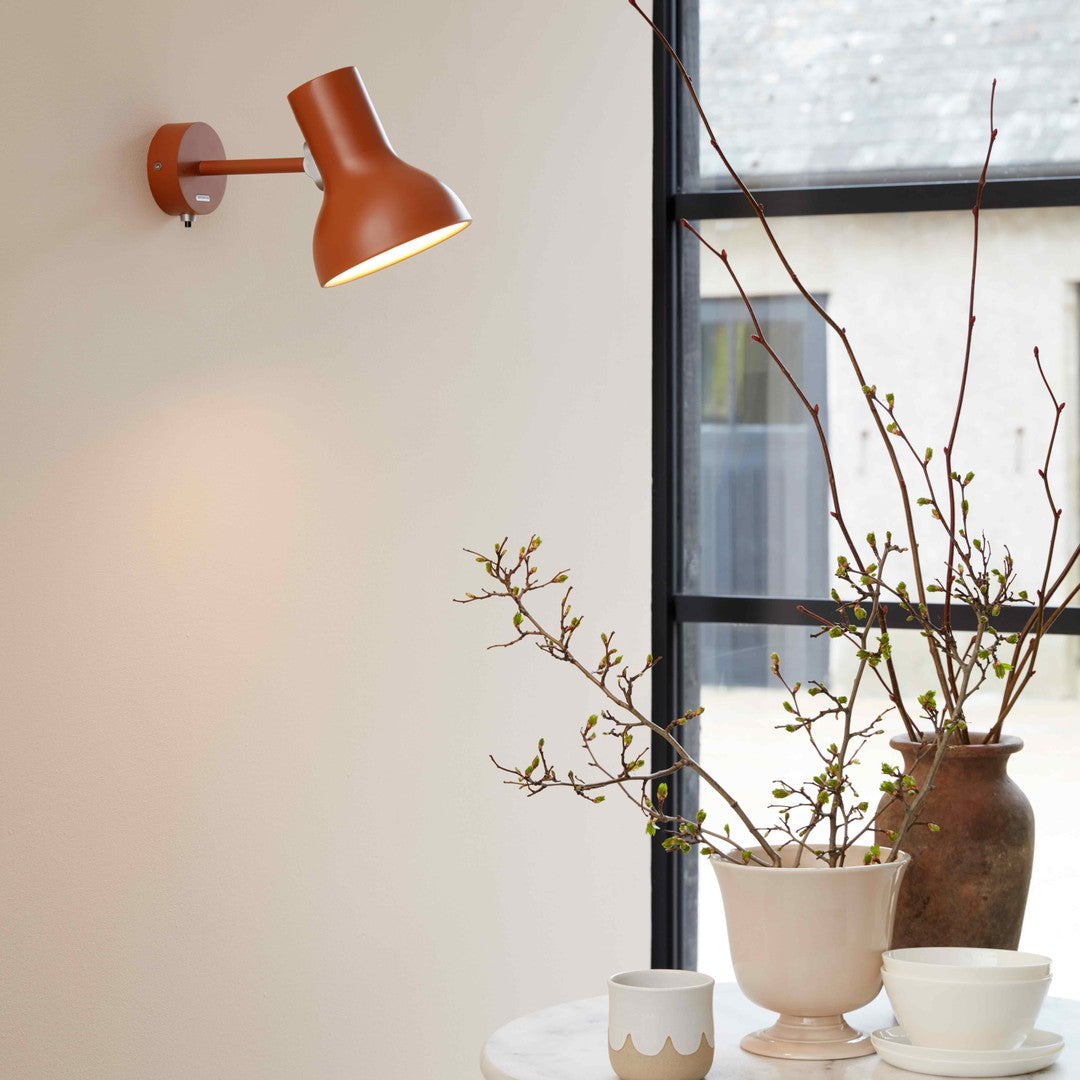 Terra-cotta wall lamp, neutral ceramic vases, and fresh green branches against a light backdrop. Elegant, modern decor.