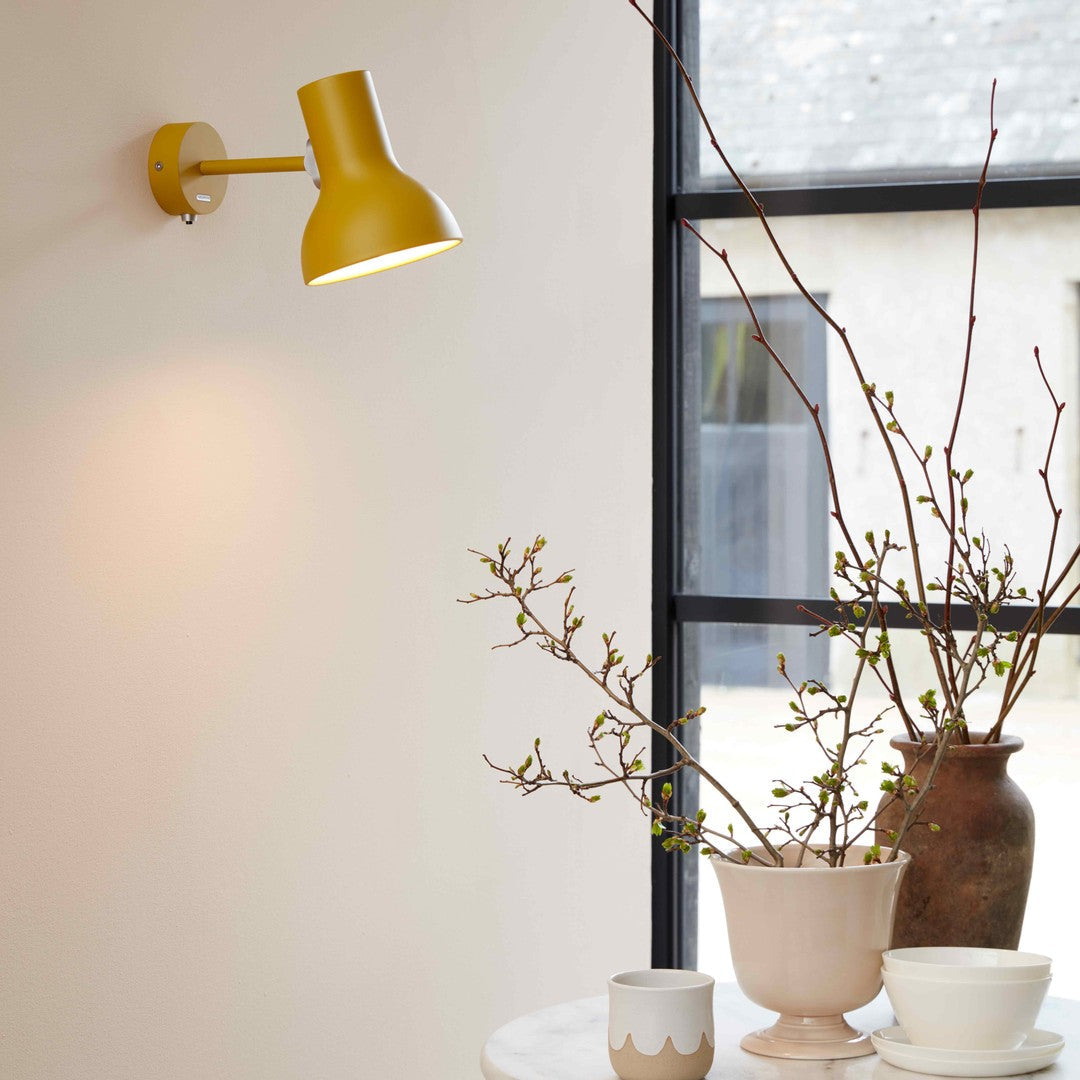 Yellow wall lamp paired with neutral-toned vases and greenery, enhancing a minimalist decor setting.