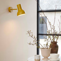 Yellow wall lamp paired with neutral-toned vases and greenery, enhancing a minimalist decor setting.