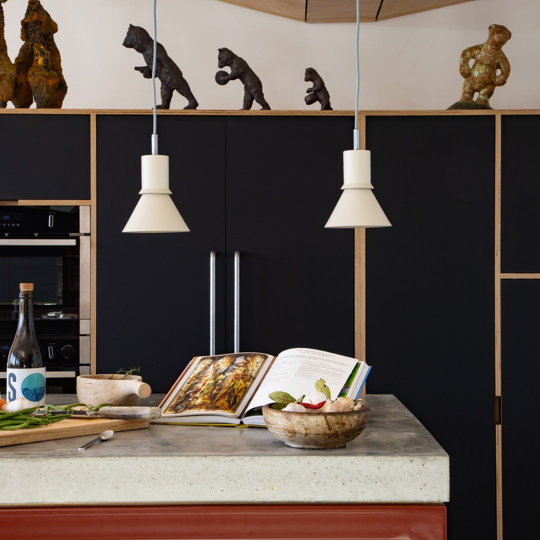 Modern kitchen scene featuring black cabinetry, white pendant lights, concrete countertop, and earthy-toned accents.