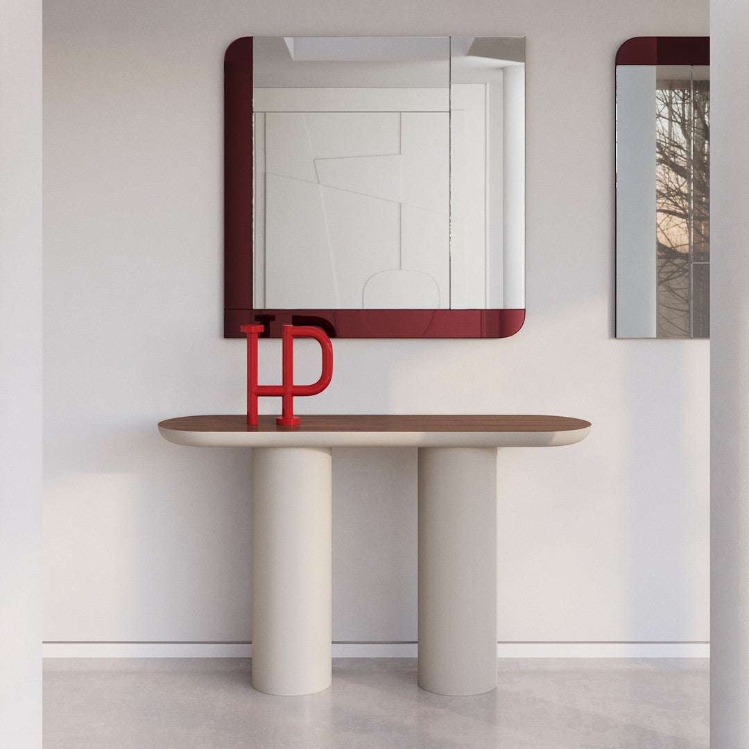 Contemporary beige console table with round legs, accented by a bold red letter and a sleek mirrored backdrop.