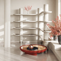 Modern white shelving unit with curved shelves, complemented by a round red coffee table and pink floral arrangement.