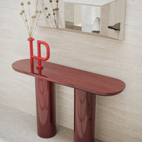Elegant burgundy console table with glossy finish and smooth contours, complemented by a bold red decorative accent.