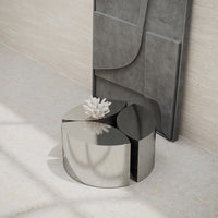 Sleek silver coffee table with geometric design, set against a textured gray wall and light stone floor.
