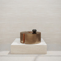 "Bronze-toned decorative piece with a smooth, sleek finish on a light stone pedestal."