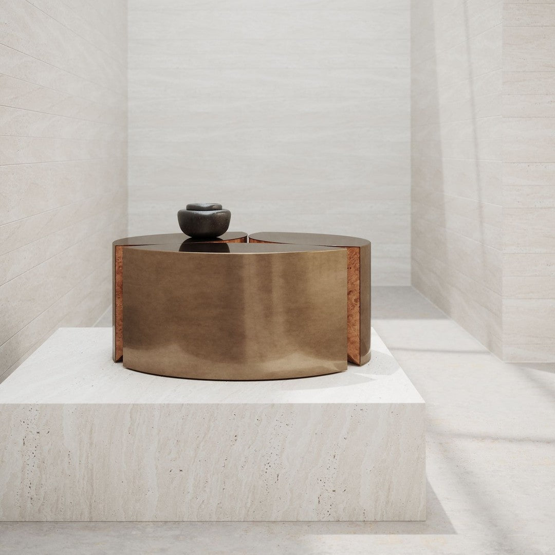 Bronze circular table with a smooth finish, contrasting against a light stone background. Simple, modern design.