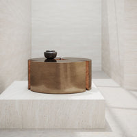 Bronze circular table with a smooth finish, contrasting against a light stone background. Simple, modern design.