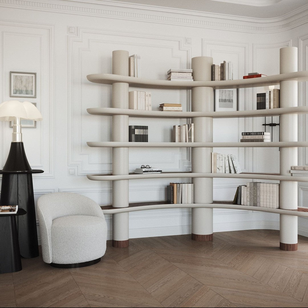 Curved beige bookshelf with smooth surfaces, accented by light wood and a neutral-toned armchair in a stylish room.