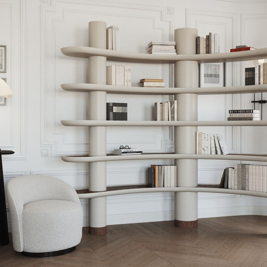 Curved beige bookshelf with light wood shelves and a textured white armchair against a neutral background.
