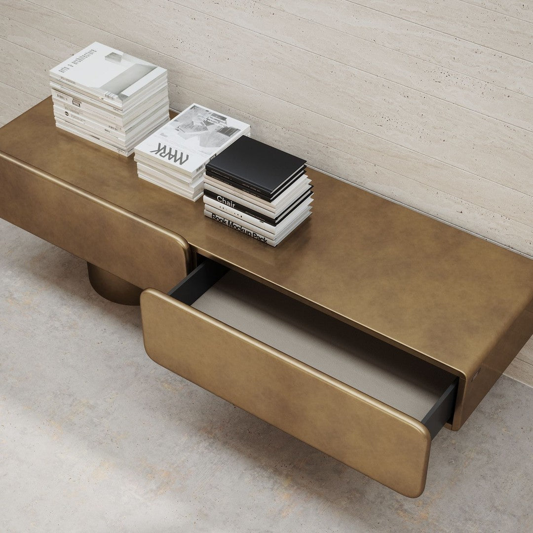 Gold-toned console table with smooth metallic finish and minimalist design, featuring two drawers and stacked books.