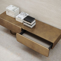 Gold-toned console table with smooth metallic finish and minimalist design, featuring two drawers and stacked books.