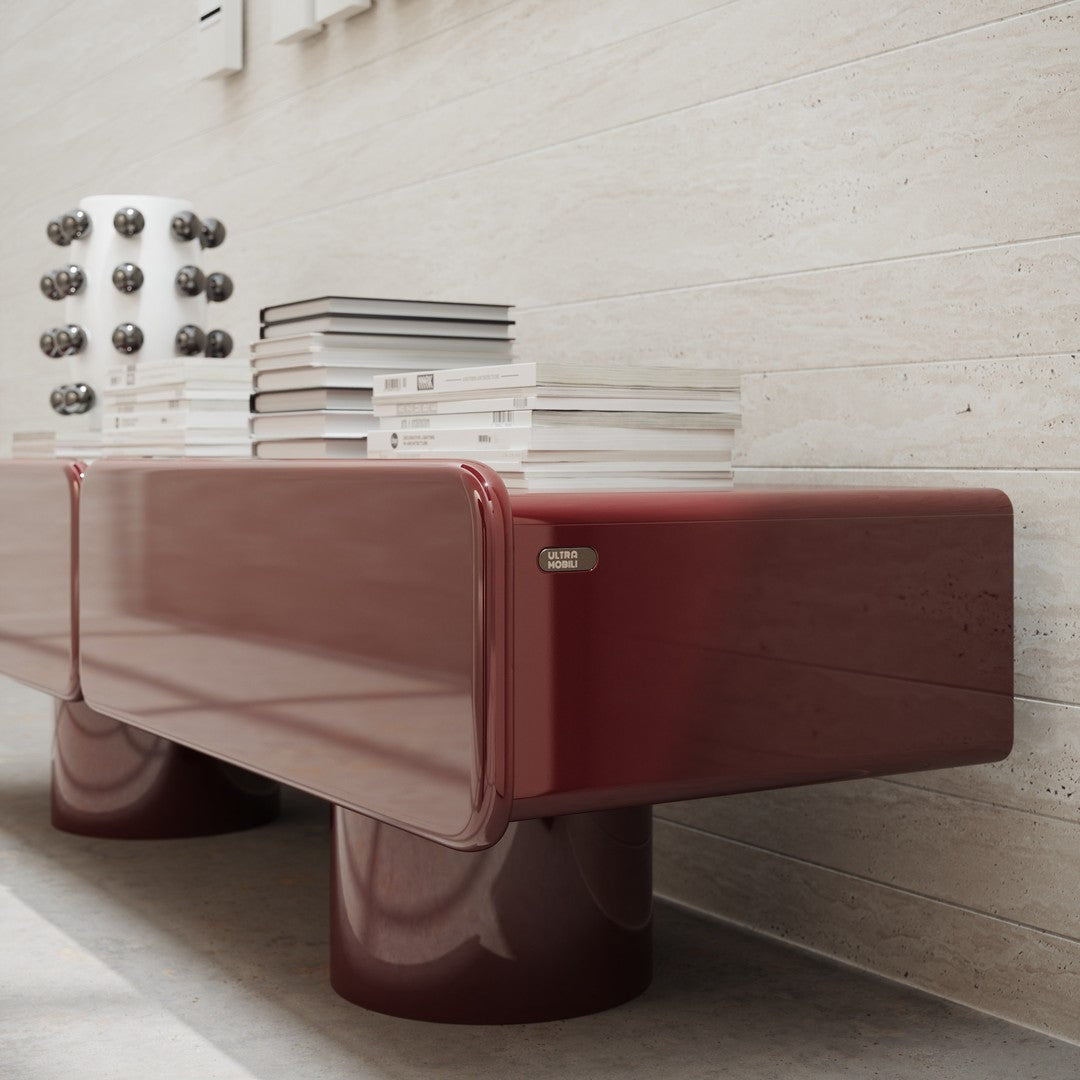 Sleek burgundy glossy console with round legs, featuring stacked clear books and decorative black and white accents.
