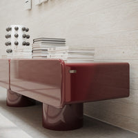 Sleek burgundy glossy console with round legs, featuring stacked clear books and decorative black and white accents.