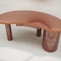 Curved brown desk with glossy finish and striped wooden accents, featuring sleek, cylindrical storage base.
