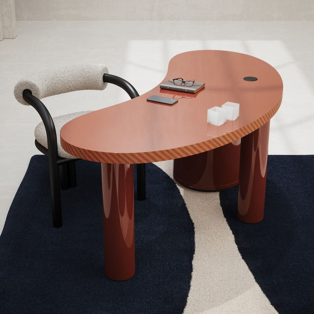 Modern kidney-shaped desk in warm terracotta with glossy finish, paired with a black and white patterned rug.