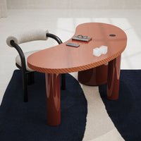 Modern kidney-shaped desk in warm terracotta with glossy finish, paired with a black and white patterned rug.