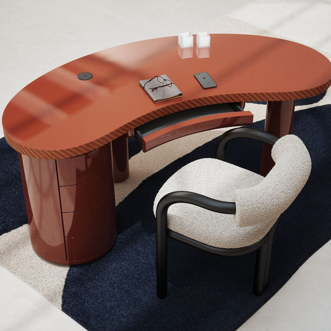 Modern oval desk in glossy terracotta with black accents, paired with a cream and black patterned chair on a navy rug.