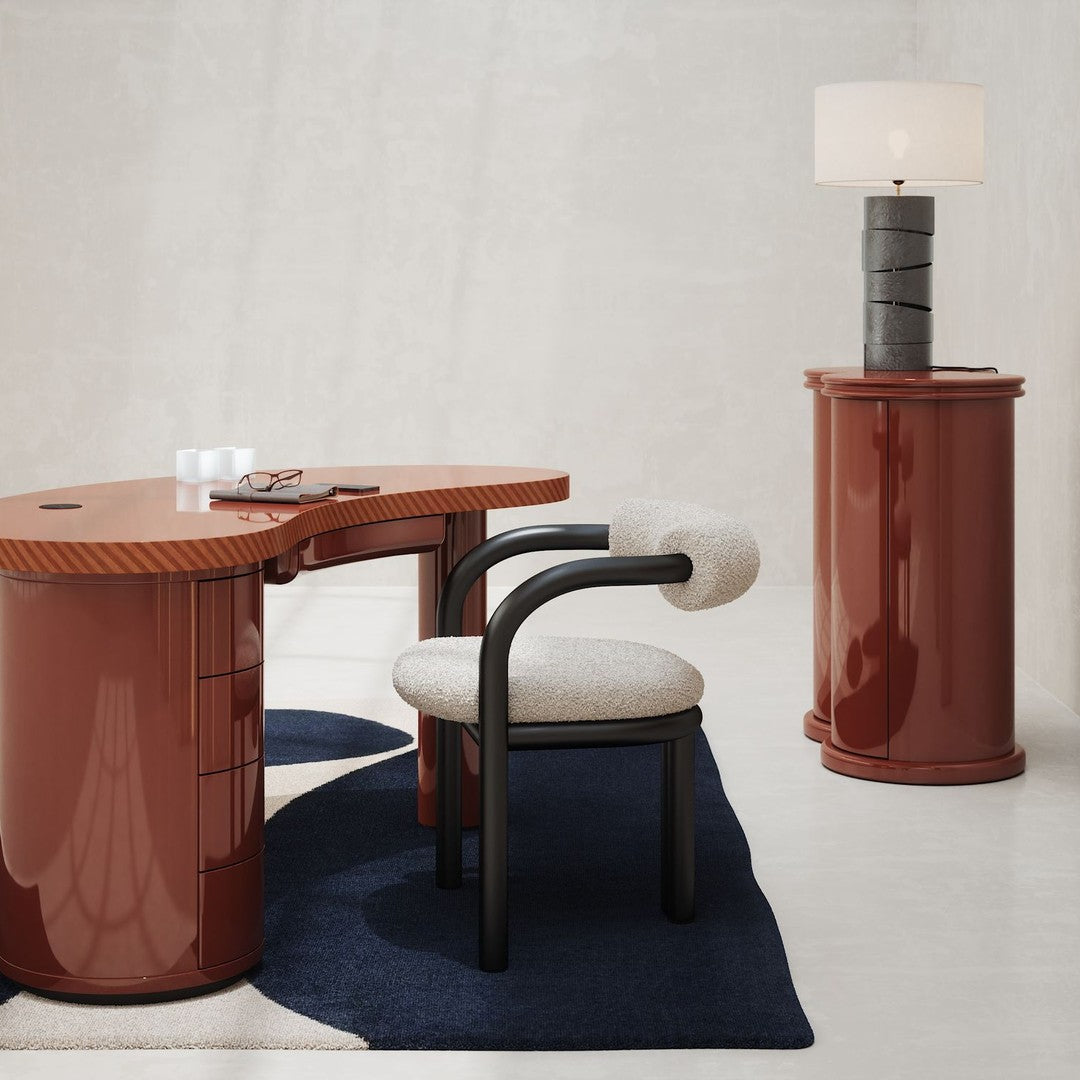 Glossy terracotta desk with ribbed accents, cream upholstered chair, and a black and white lamp on a dark blue rug.