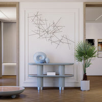 Light blue console table with metallic accents, geometric art on wall, green palm plant, and warm wood flooring.