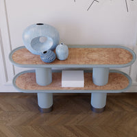 Light blue oval coffee table with textured peach top, paired with various blue vases, set against a wood floor.