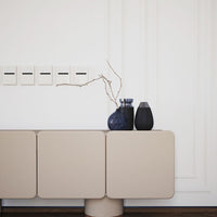 Beige modern cabinet with minimalistic design, accented by dark vases and a simple, elegant branch.