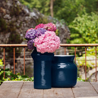 Navy blue vases with vibrant pink, purple, and lilac hydrangeas, accented against a natural green background.