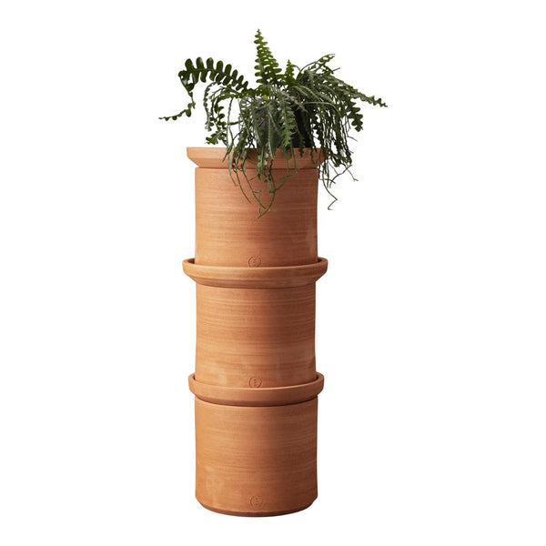 Stacked terracotta planters with a smooth, warm orange-brown finish, topped with lush green fern foliage.