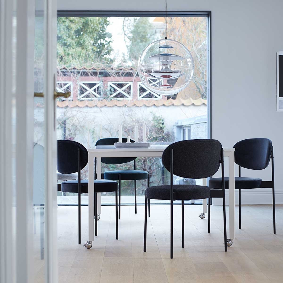 Modern dining set featuring sleek black chairs and a minimalist white table, set against a light wood floor and bright backdrop.