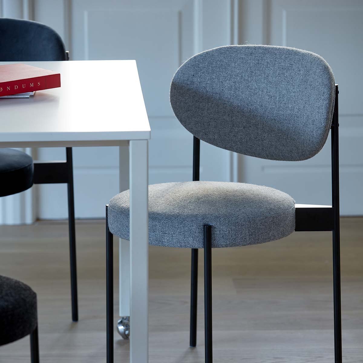 Gray upholstered chair with a sleek black frame, set beside a minimalist white table.