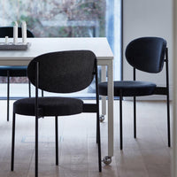 Black and charcoal upholstered chairs with sleek black metal legs against a light wooden floor. Modern minimalist design.