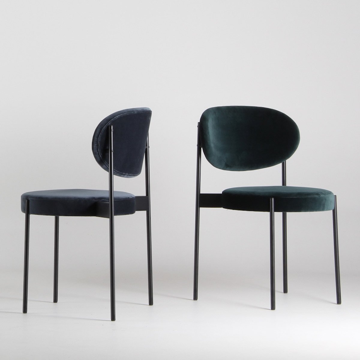 Two velvet chairs in navy blue and deep green, featuring sleek black metal legs, against a light background.