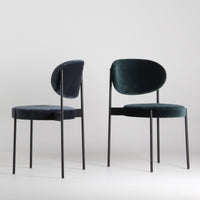 Two velvet chairs in navy blue and deep green, featuring sleek black metal legs, against a light background.