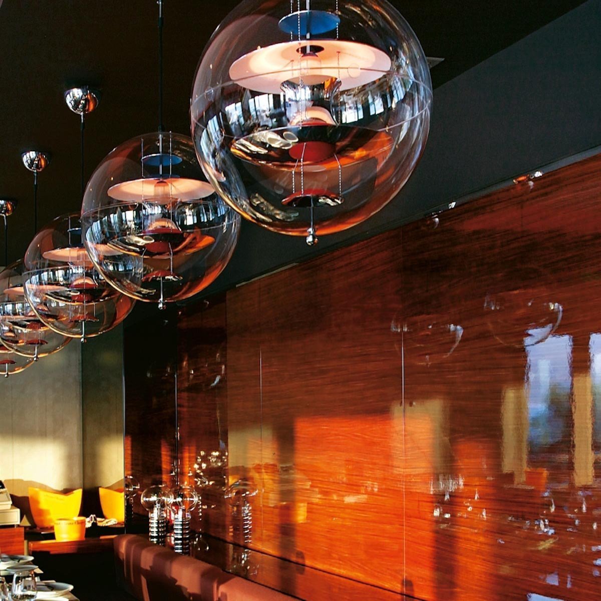 Modern pendant lights with clear glass spheres, reflecting warm amber and rich wood tones in a stylish setting.