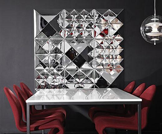 Modern silver wall display with geometric patterns, contrasting with a black background and deep red chairs.