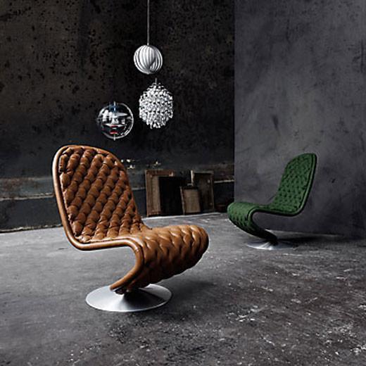 Brown tufted lounge chair and green upholstered chair with sleek metal bases, set against an industrial backdrop.