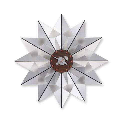 White starburst wall clock with a wooden center and orange accents, featuring sharp geometric patterns.