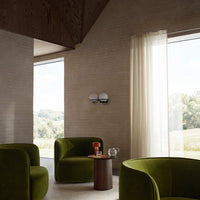 "Green velvet chairs with smooth curves in a modern, light-filled space, contrasted against soft beige walls."