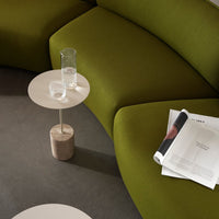 Curved olive green couch with subtle textures, paired with a minimalist white side table and stone base.