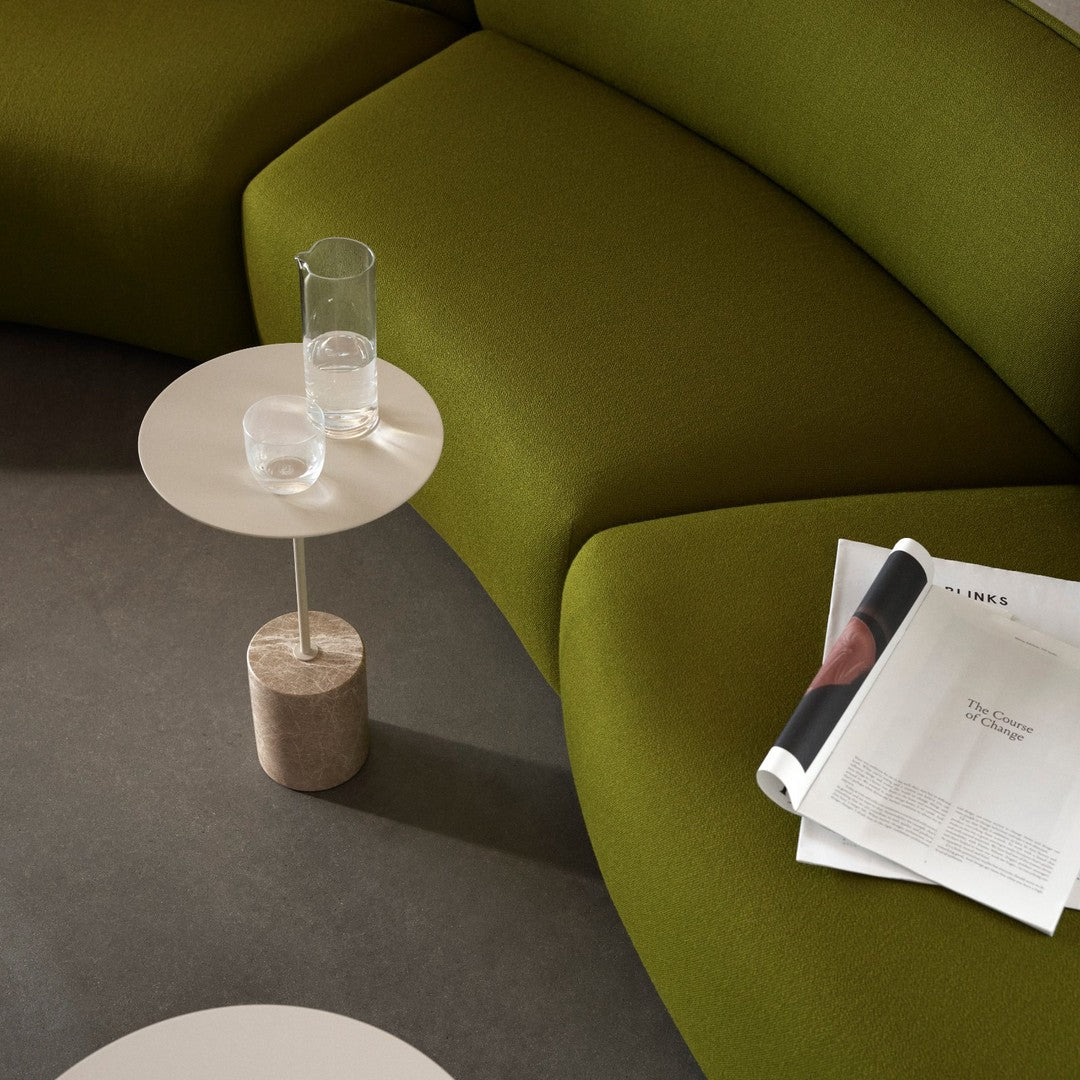 Green curved couch with smooth beige side table, showcasing modern, minimalist design and soft textures.