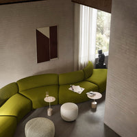 "Curved green sofa with subtle texture, paired with minimalist white and beige furniture, set in a modern interior."