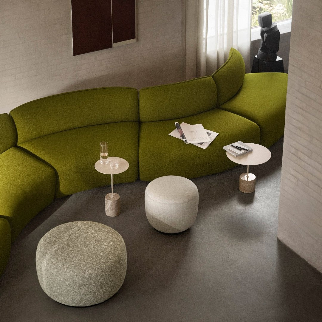 Curved green sofa with textured gray and white poufs, complemented by minimalist white and metallic accent tables.