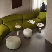 Curved green sofa with textured gray and white poufs, complemented by minimalist white and metallic accent tables.