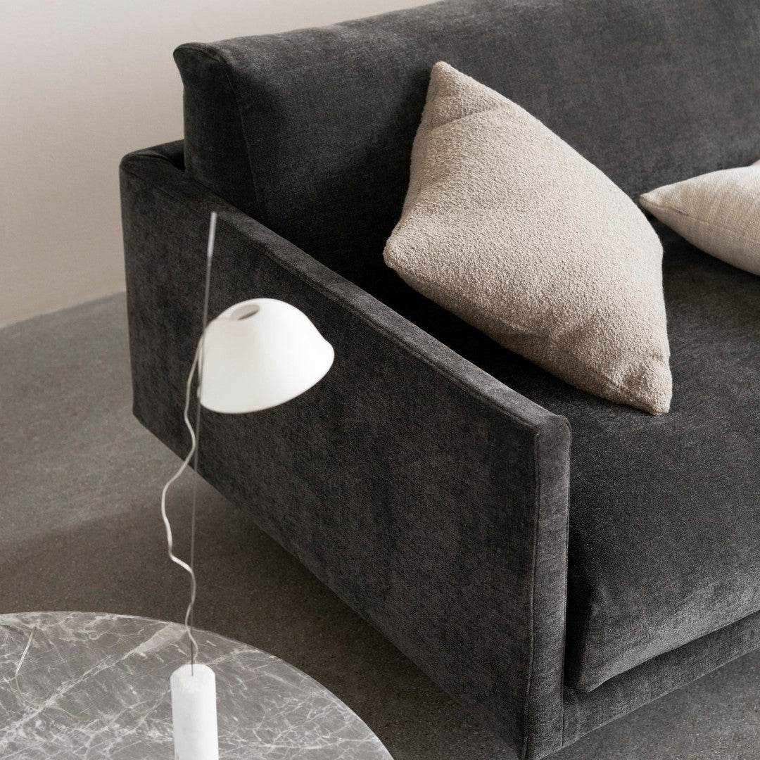 "Dark gray upholstered sofa with light beige accent pillows, alongside a marble coffee table and modern white lamp."