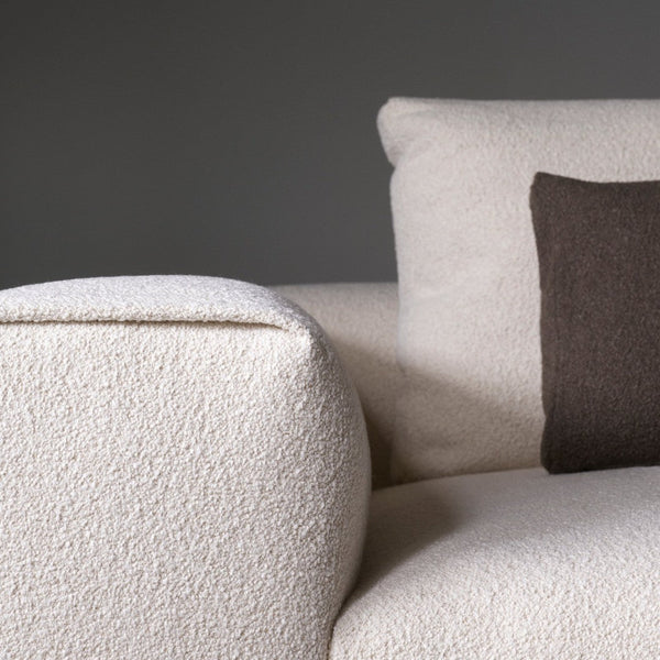 Cream textured sofa with a dark brown accent pillow against a minimalist background.