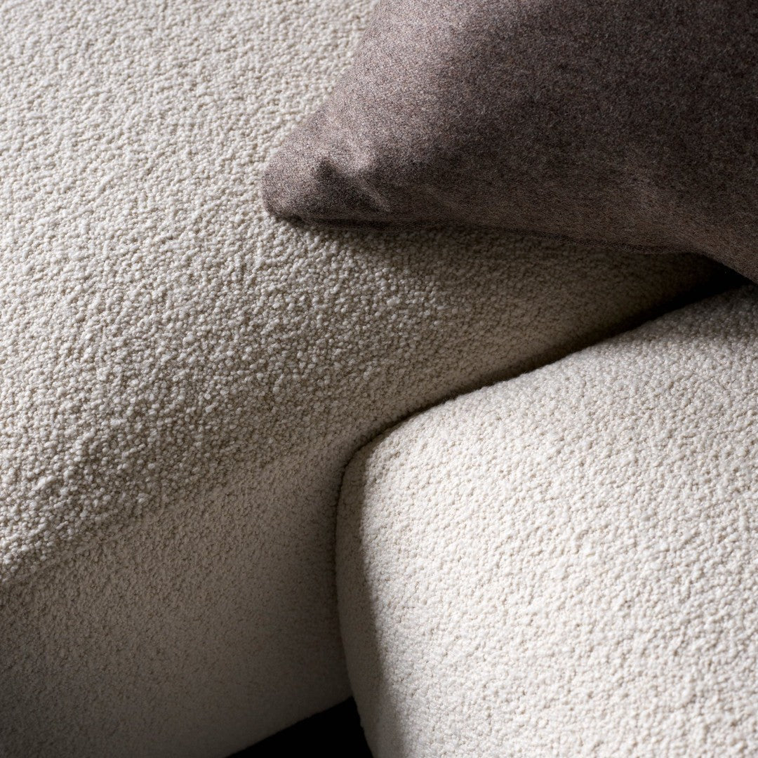 Cream textured upholstery with a subtle pattern, complemented by a soft, dark brown pillow.